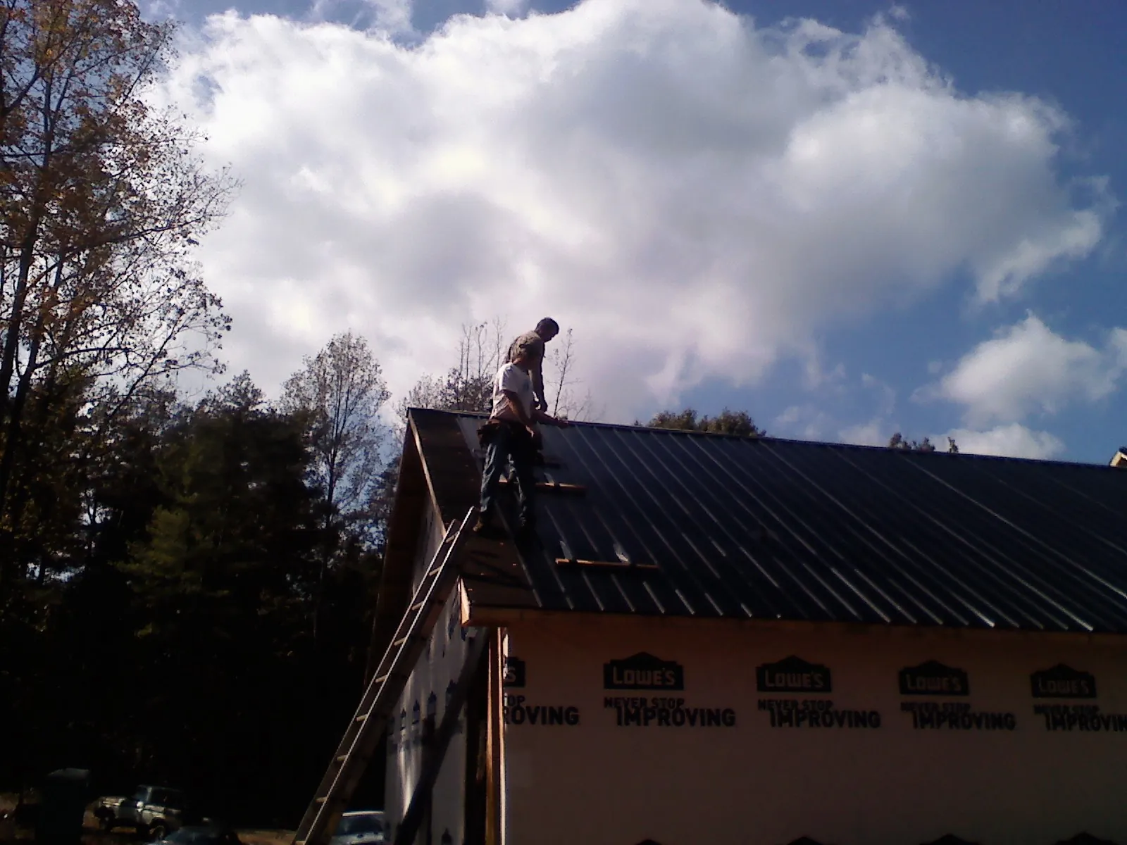 Roofer fastening dark metal panels high against a cloudy sky, from a Roof Inspection job in Plainfield