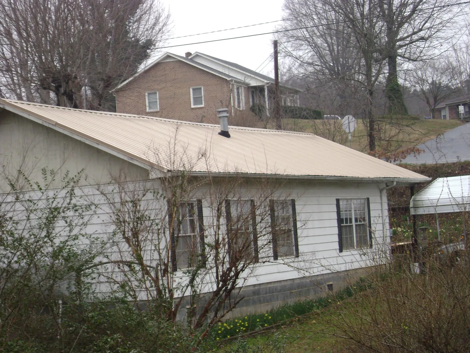 Tan metal roof on a white sided house set into a hillside — Commercial Roofing by Roofing Brothers in Plainfield